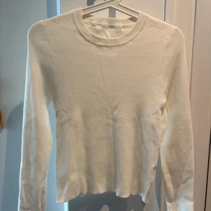 Vit stickad långärmad tröja - En stilren vit stickad tröja med rund halsringning och långa ärmar. Tröjan har en enkel och clean look som passar perfekt till jeans eller kjol. Mjuk och skön, perfekt för lager-på-lager under kyligare dagar.