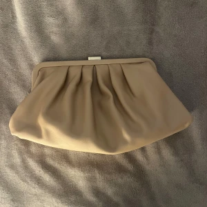 Beige handväska - Stilren beige kuvertväska. Väskan har både en avtagbar axelrem i matchande beige och en chunky silverfärgad kedja, så du kan bära den på flera sätt. Inga defekter💕😊