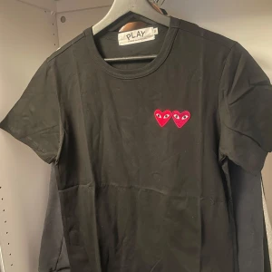 Cdg tshirt - Svart t-shirt från Comme des Garçons Play med två röda hjärtan med ögon broderade på bröstet. Klassisk rund halsringning och korta ärmar. Tillverkad i mjuk bomull för en skön känsla och clean look. Helt ny Tisha som endast är testad. Säljs då jag inte tyckte den passade mig. Storlek M