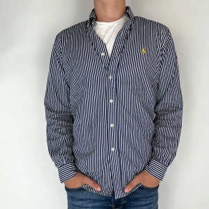 Ralph Lauren Skjorta  - Nu har vi nöjet att erbjuda en klassisk  skjorta från det välkända varumärket Ralph Lauren. Plagget är i storlek Medium och är i mycket gott skick, utan några synliga defekter. Modellen på bilden är 182 cm lång och väger 75 kg, vilket kan ge en god indikation på tröjans passform.
