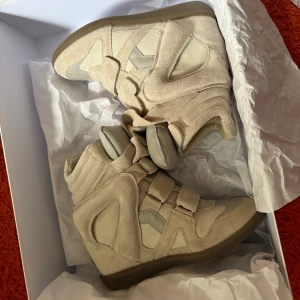Beige wedge sneakers Isabel Marant - Snygga beige wedge sneakers från Isabel Marant i mocka och skinn. Skorna har coola paneler, kardborreband och hög plattformssula. Perfekta för dig som vill ha en sportig men ändå trendig look med extra höjd.