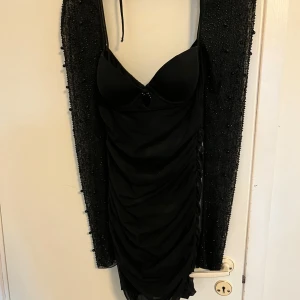 Svart kort klänning från Oh Polly - Supersnygg svart kort klänning från Oh Polly med draperad effekt och smala axelband. Klänningen har vadderade kupor och dragkedja  för en tight passform. Perfekt för dig som vill sticka ut med en elegant och trendig look.