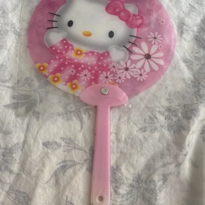 Hello Kitty rosa solfjäder - Tre söta rosa solfjädrar med Hello Kitty-motiv. Varje solfjäder har olika tryck med blommor, rosetter och frukter. Rund form, plastmaterial och handtag i ljusrosa. Perfekt accessoar för varma dagar eller som kawaii-inredning. 49kr/st . Helt ny , finns fler kvar 