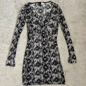 Svartvit mönstrad klänning H&M Divided - Tight svartvit kortklänning från H&M Divided med lång ärm och djup v-ringning. Klänningen har ett fint mönster och väldigt skönt och tung material. Perfekt för dig som gillar att festa- den här klänningen är super fin OCH bekväm! Den sitter super fint 