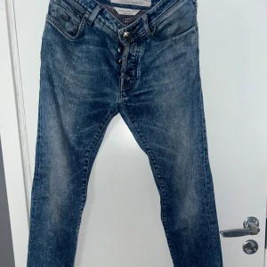  Jacob Cohen Jeans 688 - Snygga blå jeans från Jacob Cohen med en klassisk femficksdesign och knappgylf. Jeansen har en lätt tvättad look och en broderad logga på baksidan. Perfekta för en avslappnad stil. (Sliten logga, Modell 688)