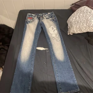 Blå jeans med broderad design - Snygga blå jeans med en unik broderad design på framsidan. De har en klassisk femficksmodell och en cool tvättad look. Perfekta för att ge din outfit en extra edge.