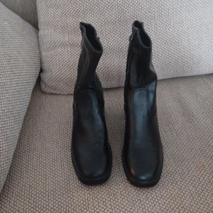 Svarta boots från Tamaris - Snygga svarta boots från Tamaris i skinn med dragkedja på sidan. De har en klack och en rund tå, vilket ger en stilren look. Perfekta för att komplettera din outfit med en touch av elegans.