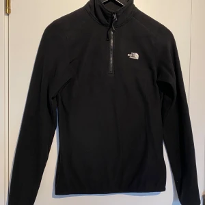 Svart fleece tröja/jacka  från The North Face - Säljer en svart fleece tröja från The North Face med halv dragkedja och broderad logga på bröstet. Perfekt för kyliga dagar och utomhusaktiviteter. Tröjan har långa ärmar och en hög krage för extra värme. Är i jättefint då jag endast har använt denna vid 2 tillfällen. Inga skador eller anmärkningar. Nyskick! 