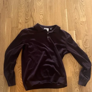 Vinröd långärmad pikétröja - Snygg vinröd pikétröja med långa ärmar och klassisk krage. Perfekt för en stilren look. Tröjan har knappar vid halsen för en justerbar passform.