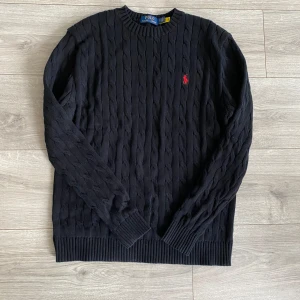  kabelstickad Polo Ralph Lauren - Säljer en stilren svart kabelstickad tröja från Polo Ralph Lauren. Tröjan har en klassisk rund halsringning och ett rött broderat märke på bröstet. Kontakta vid minsta fundering🙌