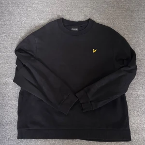 Svart sweatshirt från Lyle & Scott - Säljer en svart sweatshirt från Lyle & Scott med deras ikoniska logga på bröstet och text på ärmarna. Tröjan har långa ärmar och ribbade muddar. Perfekt för en casual look.