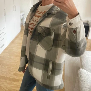 Rutig overshirt från Rising - Snygg rutig overshirt i gröna och vita toner från Rising. Jackan har långa ärmar och knappar framtill samt praktiska fickor. Perfekt för lager-på-lager-stil.