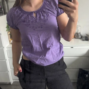Lila blus med broderi - Säljer en söt lila blus med korta ärmar och vackert broderi vid halsringningen. (Katt och kanin finns i hemmet) 