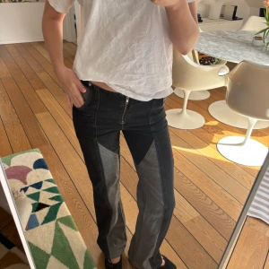 Unika coola jeans  - Snygga svarta jeans med kontrasterande grå paneler och dragkedja fram köpt vintage. De har en unik design med låg midja och raka ben. Perfekta för en trendig look. Midjemått storlek 26