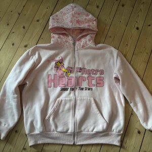 Rosa hoodie från Retro Hearts ”Shoot For The Stars”!!! - Säljer en söt rosa hoodie från Retro Hearts med dragkedja och en cool illustration på framsidan. Hoodien har en mönstrad huva med stjärnor och  fickor framtill. Jätte söt och cool funkar för män och kvinnor, fått så många komplimanger dom få gångerna jag använt den. Super bra skick
