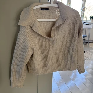Beige stickad tröja från Gina Tricot - Säljer en mysig beige stickad tröja från Gina Tricot. Tröjan har en bred krage och långa ärmar, perfekt för kyliga dagar. Den ribbade strukturen ger en stilren look. Passar utmärkt till både jeans och kjol.