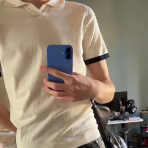 Vit pikétröja med svarta detaljer - Säljer en stilren vit pikétröja med svarta detaljer på ärmsluten. Perfekt för en avslappnad men ändå snygg look. Tröjan har en klassisk krage och korta ärmar. Storlek L men passar M