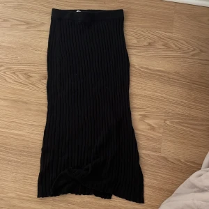 Svart ribbad kjol från Gina Tricot - Snygg svart ribbad kjol från Gina Tricot i storlek S. Kjolen har en stilren design med en slits som ger extra rörelsefrihet. Perfekt för att skapa en chic look.