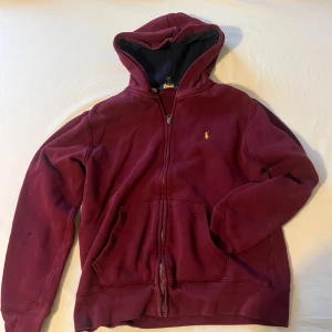 Vin röd Ralph lauren zip up hoodie - Väldigt fin och stilren vin röd Ralph lauren zip up hoodie med gult märke. Den är i bra skick och passar både kyla och värme. Litet hål på höger arm annars i bra skick hör av dig om du vill bättre bilder eller bara allmäna frågor!