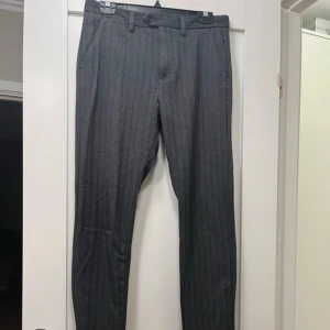 Grå kostymbyxor från Jack & Jones - Snygga grå kostymbyxor från Jack & Jones med slim passform. Byxorna har ett diskret randigt mönster.