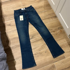 Blå bootcut jeans - Snygga blå bootcut jeans med klassisk femficksdesign och läderdetalj vid midjan. Perfekta för en avslappnad stil med en touch av retro. Passar bra till både sneakers och stövlar.
