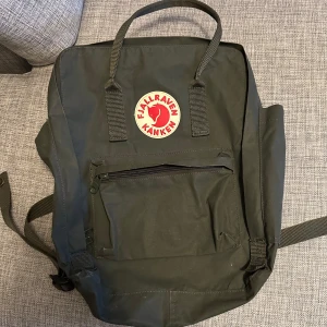 Grön ryggsäck från Fjällräven - Säljer en klassisk grön Fjällräven Kånken ryggsäck. Den har ett stort huvudfack, en mindre framficka med dragkedja och justerbara axelremmar. Perfekt för både vardag och äventyr. Säljer den då jag inte har någon användning av den. 