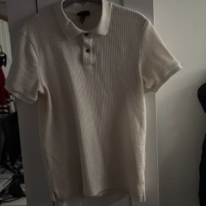Vit H&M pikétröja  - Säljer en stilren vit pikétröja från H&M i slim fit. Tröjan har korta ärmar och en klassisk krage med knappar framtill. Perfekt för en avslappnad men ändå snygg look.