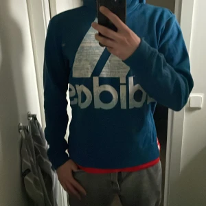 Blå hoodie från Adidas - Säljer en blå hoodie från Adidas med stor logga på framsidan. Tröjan har långa ärmar och en klassisk huva. Perfekt för en avslappnad stil eller träning. Hör av dig vid intresse! 💙