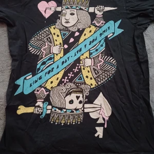 Svart t-shirt med spelkortstryck från Bowery - Cool svart t-shirt från Bowery med ett unikt spelkortstryck i rosa, blått och gult. Designen visar en kung med ett hjärta och texten 'King for a day'. Perfekt för dig som vill sticka ut med en lekfull stil.