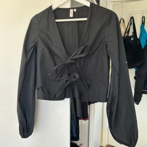 Svart knytblus från Nelly - Säljer en svart blus från Nelly med knytning framtill. Blusen har långa ärmar och en v-ringad design💕