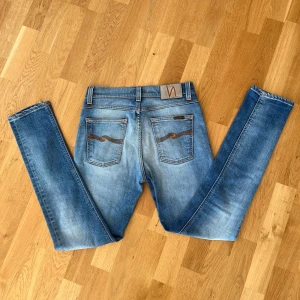 Blå Nudie jeans Lean Dean  - Snygga blå jeans från Nudie Jeans med klassisk femficksdesign och orangea sömmar på bakfickorna. De har en dragkedjegylf  och är tillverkade i slitstarkt denim. Modellen är Lean Dean. Perfekta för en avslappnad stil.