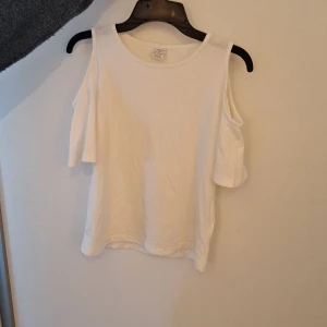 Vit topp  - Säljer en stilren vit topp från Lindex med offshoulder-design. Perfekt för varma dagar med sin luftiga passform. Tillverkad i ett mjukt material som känns skönt mot huden.