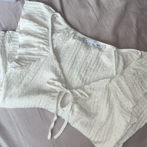 Vit blus/topp - Supersöt vit blus från 157 med volangärmar och v-ringning. Toppen har knyt framtill och är gjord i ett lätt, krinklat tyg som ger en luftig känsla. Storlek L och säljs då jag har den i svart också som jag trivs bättre i så den är knappt använd. Står ej för frakten