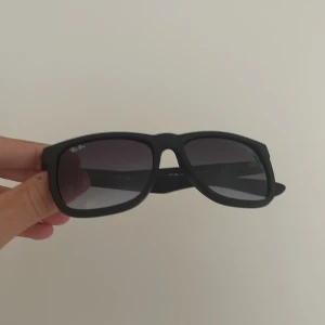 Svarta solglasögon från Ray-Ban - Snygga svarta solglasögon från Ray-Ban med mattsvart båge och fyrkantig form. Glasen är mörka och ger en cool vibe. Klassisk Ray-Ban-logga på både lins och skalmar. Perfekta för att lyfta din stil i sommar.
