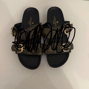  sandaler  - Snygga sandaler med klassiskt brunt  och två breda remmar med guldfärgade spännen. Svart sula och öppen tå ger en clean look. Perfekta för sommaren och riktigt lyxig känsla.