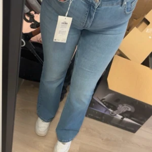 Ljusblå bootcut jeans med fickdetalj - Säljer ett par ljusblå jeans med bootcut passform och hög midja. Jeansen har en snygg ficka med knapp bak och klassisk femficksdesign. Tillverkade i mjukt denimtyg som sitter skönt och ger en avslappnad vibe.