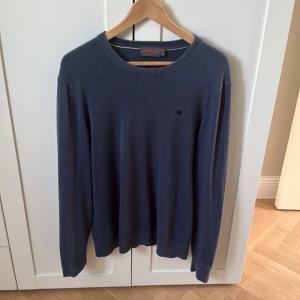 Blå långärmad tröja Morris - Snygg blå tröja från Morris med rund halsringning och diskret broderad logga på bröstet. Långärmad modell i mjukt material som passar perfekt till jeans eller chinos. Enkel och stilren design som funkar till många olika looks.