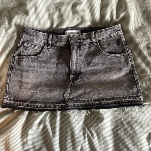 Grå jeanskjol från Pull&Bear - Säljer en grå, tvättad jeanskjol från Pull&Bear. Kjolen är kort med rå, fransig fåll och har en cool, lite sliten look. 