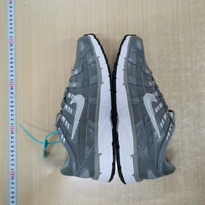 Nike grå sneakers med vit sula# p-6000 - Snygga grå Nike sneakers med vit och svart sula. Skorna har meshpaneler för extra andningsförmåga, silverfärgade detaljer och klassisk Nike Swoosh på sidan. Perfekta för dig som gillar sportig stil och vill ha bekväma skor till vardags.