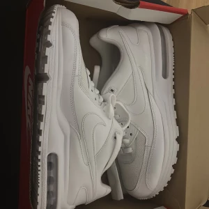 Vita Nike Air Max sneakers - Fräscha helvita Nike Air Max sneakers med klassisk luftsula och snygg design. Skorna har en blandning av skinn och mesh, vilket ger både stil och bra andningsförmåga. Perfekta för dig som vill ha en clean look och bekväma skor till vardags.
