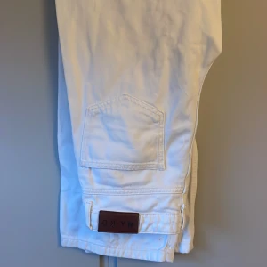 Vita raka jeans från NA-KD, strl 36 - Snygga vita jeans från NA-KD i rak modell med hög midja. Klassisk femficksdesign, silverfärgade nitar och knapp, samt NA-KD-lapp bak. Tillverkade i bomull för en skön och stilren look.