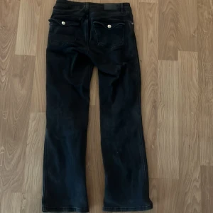 Svarta utsvängda jeans från Lager157 - Svarta jeans från Levis med raka ben och klassisk femficksdesign. Jeansen har silverfärgade knappar och detaljer, samt en enkel och stilren look. Perfekta för dig som gillar en tidlös och clean stil.