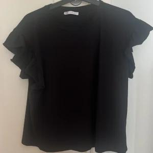 Svart volangblus från Zara - Supersnygg svart tröja från Zara med volangdetaljer på ärmarna. Använd en gång 