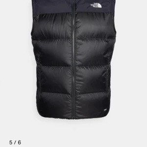 Svart dunväst från The North Face - Snygg svart dunväst från The North Face med en modern design och dragkedja framtill. Västen har en diskret logga på bröstet. Perfekt att slänga över en hoodie för extra värme. Klassisk och stilren look.👀 Pris kan diskuteras. Skicka för fler bilder. Det finnns på små hål på ryggen men som är enkla att fixa med lite lim.