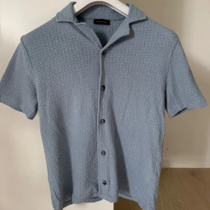 Blå kortärmad skjorta Oscar Jacobson - Snygg ljusblå skjorta från Oscar Jacobson i storlek S. Enkel och stilren design som passar till många tillfällen. Den är som ny då den endast är använd 1 gång och säljs pga den är för liten. Vid funderingar eller fler bilder är det bara att skriva🙌