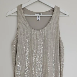 Champagnefärgad paljettklänning - Champagnefärgad paljettklänning från H&M. Rak modell med rund halsringning.  Använd få gånger, mycket fint skick Storlek S