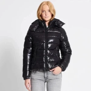 Lager 157 pufferjacka   - Säljer en svart glansig pufferjacka med huva och dragkedja framtill. Jackan har en quiltad look och är perfekt för kalla dagar. Den har lång ärm och en klassisk, lite boxig passform. Snygg och enkel att styla till jeans eller andra byxor.