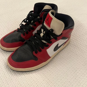Nike Air Jordan 1 Chicago Highs 42 - Säljer ett par ikoniska Nike Air Jordan 1 Highs i Chicago-färg. Skorna har svart, rött och vitt skinn, svart swoosh och klassisk Air Jordan-logga på sidan. Svart snörning och vit mellansula med svart yttersula. Perfekta för dig som vill sticka ut med en tidlös sneaker.