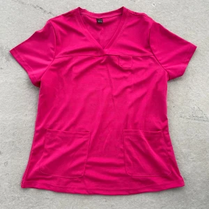 Rosa kortärmad topp från SHEIN - En starkt rosa topp från SHEIN i storlek XL. Modellen har v-ringning, korta ärmar och tre praktiska fickor framtill. Tillverkad i mjukt syntetmaterial som känns skönt mot huden. Perfekt för dig som gillar färg och enkel stil.