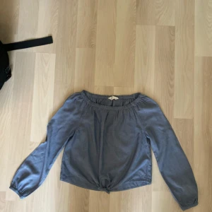 Blå offshoulder blus med knyt - Snygg blå blus med offshoulder-modell och långa ärmar. Toppen har en elastisk kant upptill och en knutdetalj framtill som ger en chill vibe. Perfekt till jeans eller kjol för en avslappnad look.